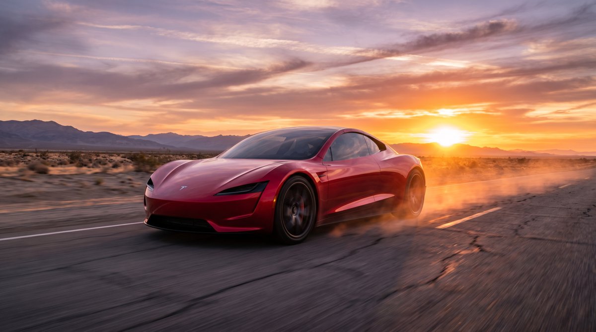 A sleek red Tesla Roadster sports car on a desert highway at sunset